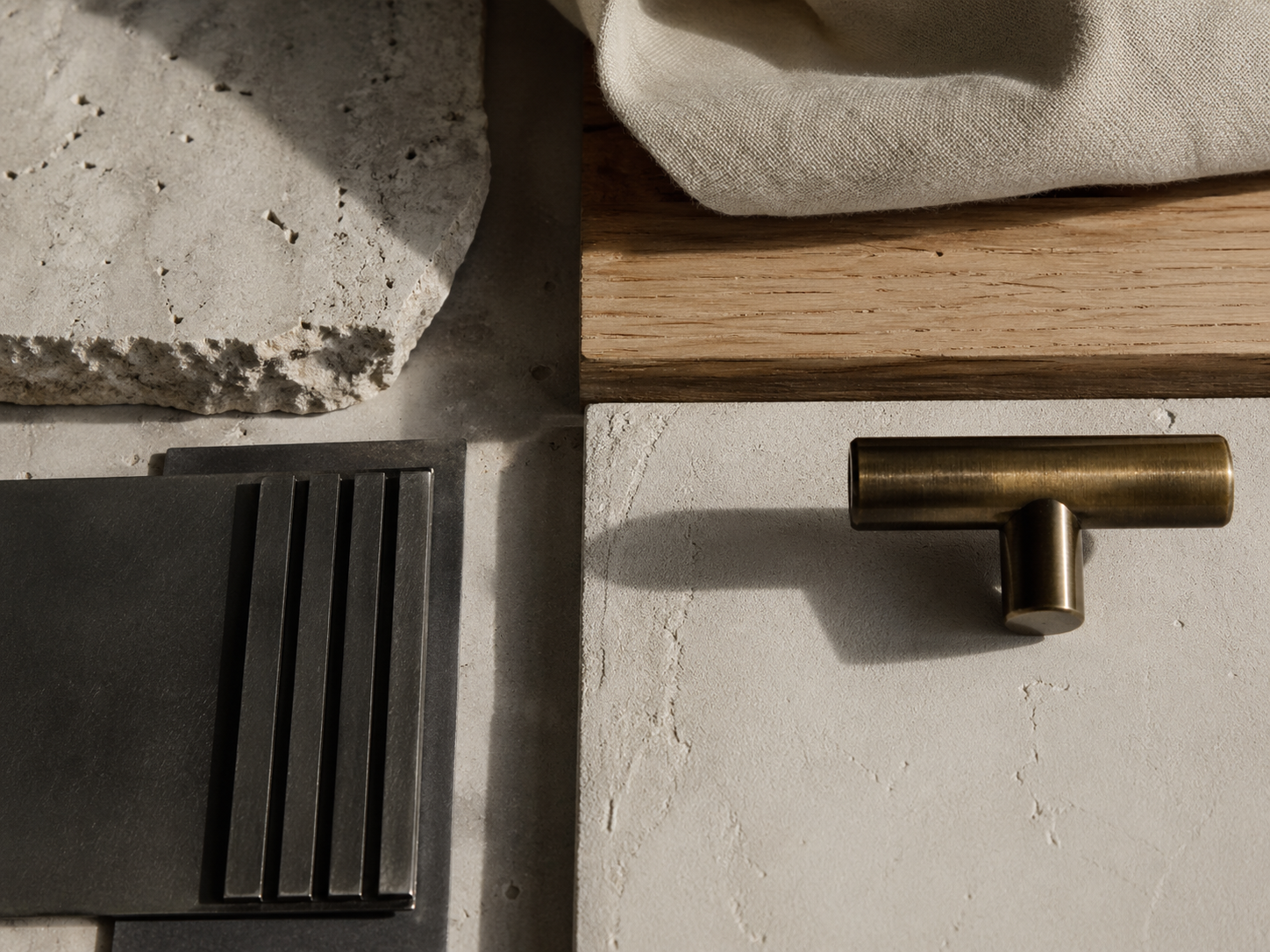 Close-up arrangement of stone, timber, fabric, black metal and brass hardware